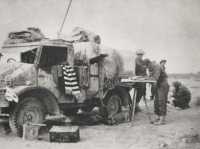 An artillery signals truck 
in action, with one man busy at the map board; behind him another crouches at the telephone