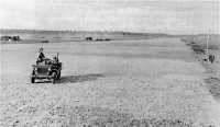 A jeep speeds a 
maintenance crew to duty along the runway improved and extended by the Americans