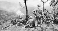 Pushing to Yae-Take, 
infantrymen of the 6th Marine Division pause on a mountain top while artillery shells a Japanese position