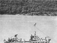 A workman strings a ferry 
cable across the Salween while men in the foreground build the ferry